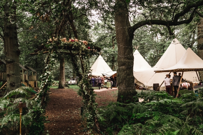 Rustic arch decorated with LED lights, trailing ivy and flowers at a woodland Tipi wedding